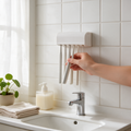 A hand takes a toothbrush from a white wall-mounted holder
