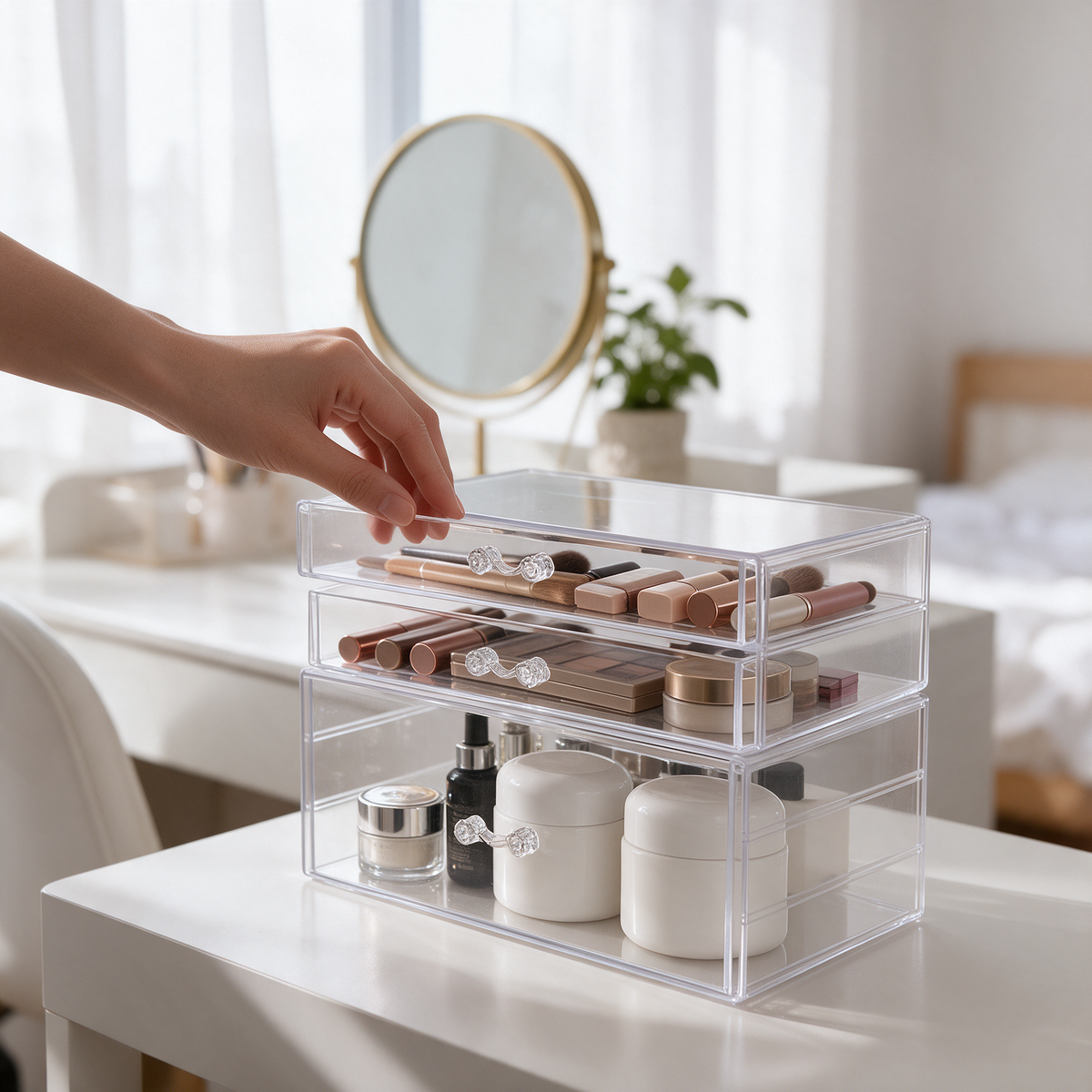A hand opens a clear makeup organizer drawer on a white vanity